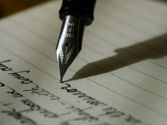 The nib of a fountain pen on paper with cursive on the paper.